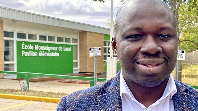 Gros plan de Ronald Ajavon devant la façade de l'École Monseigneur de Laval, à Regina.