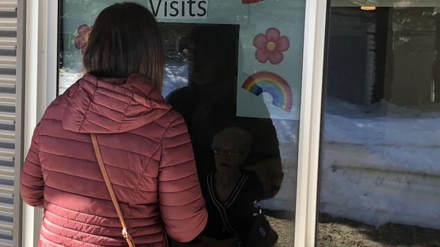 Une femme à l'extérieur devant une fenêtre parle à sa mère qui se trouve de l'autre côté à l'intérieur de l'édifice.