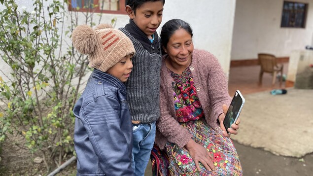 Deux enfants, ainsi que leur mère, parlent à leur père par vidéoconférence.