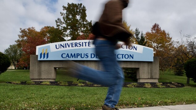 Un homme passe en courant devant l'enseigne du campus de Moncton.