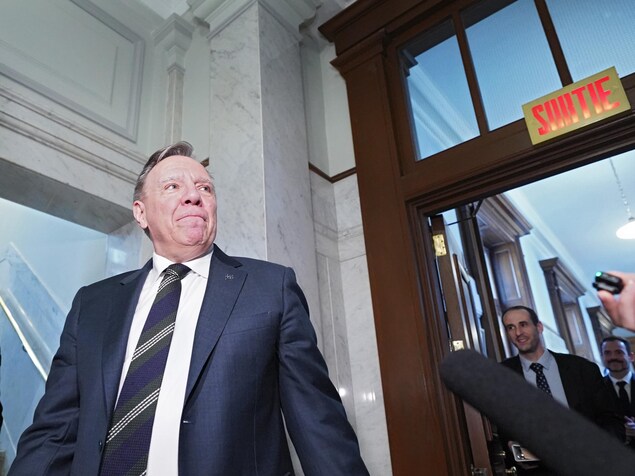 François Legault regarde à sa gauche, où l'on voit une enseigne «Sortie».