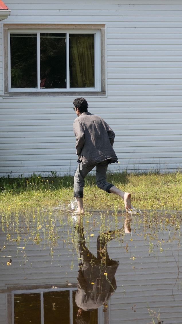 Un homme pieds nus courre vers sa maison sur un terrain inondé.