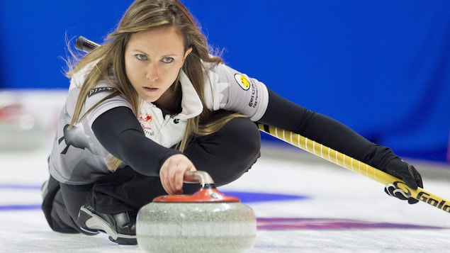 La joueuse qui glisse sur la glace avec une pierre de curling La joueuse qui glisse sur la glace avec une pierre de curling