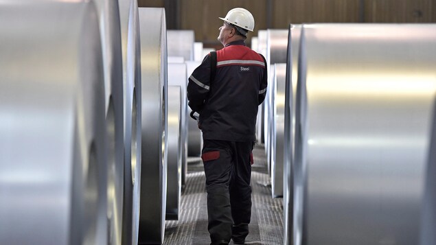 Un travailleur marche entre des rangées de bobines d'acier.
