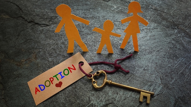 Représentation d'une famille en figurines de papier, placées tout près d'une clé de maison familiale et d'une étiquette portant la mention Adoption.