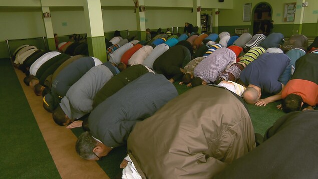 Des hommes agenouillés, têtes baissées faisant la prière.