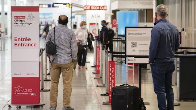 Des voyageurs attendent près d'une clinique de dépistage à l'aéroport international Pierre-Elliott-Trudeau de Montréal.