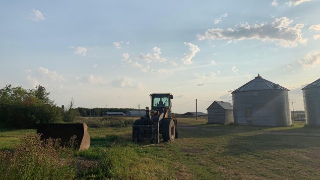 L'arrière court d’une ferme, un tracteur au centre de l'image et de petits silos à grains sur la droite. 