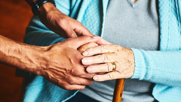 Une main d'homme tient la main d'une femme âgée tenant une canne.