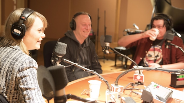 Les trois sont assis à une table ronde, derrière des micros.