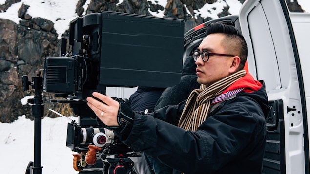 Le cinéaste Anh Minh Truong regarde dans une grosse caméra. 