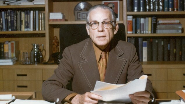 Le Dr Armand Frappier s'adressant à la caméra, feuilles de papier à la main, dans les années 1970.