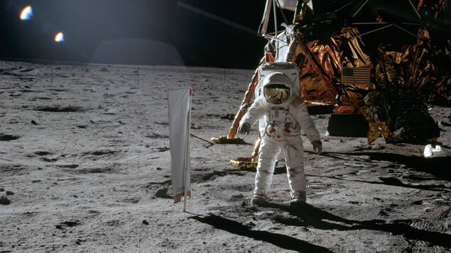 L'astronaute Buzz Aldrin se tient à proximité du capteur de vent solaire qu'il a déployé sur la lune, le module lunaire est visible en arrière plan.
