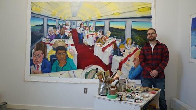 L'artiste Evin Collis pose devant un de ces tableaux où l'on voit les gens qui voyagent assis dans un train.