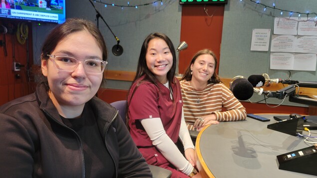 Trois jeunes femmes dans un studio de radio, souriantes.