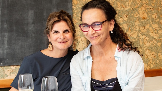 Les deux femmes posent en souriant, un verre de vin à la main.