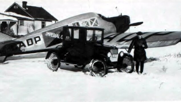 Une ancienne photo d'un homme appuyé sur une voiture devant un avion en métal.