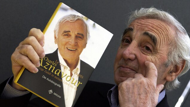 Charles Aznavour se pointe le visage en posant avec son autobiographie en langue allemande. Charles Aznavour se pointe le visage en posant avec son autobiographie en langue allemande.