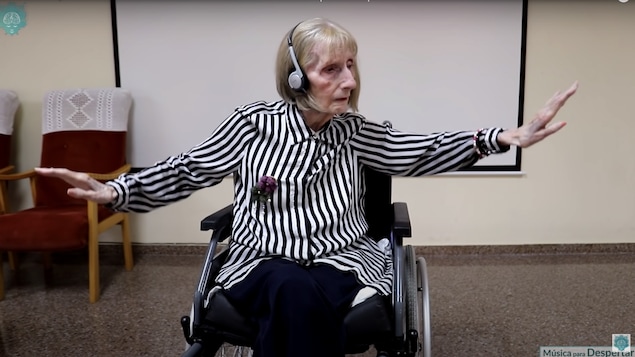Une femme âgée assise dans un fauteuil roulant, les bras étendus dans les airs avec grâce.