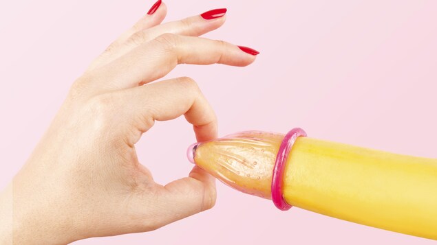 Une main de femme avec des ongles rouges met un condom sur une banane. La grande majorité des cas rapportés de syphilis, soit 95 %, sont des hommes.