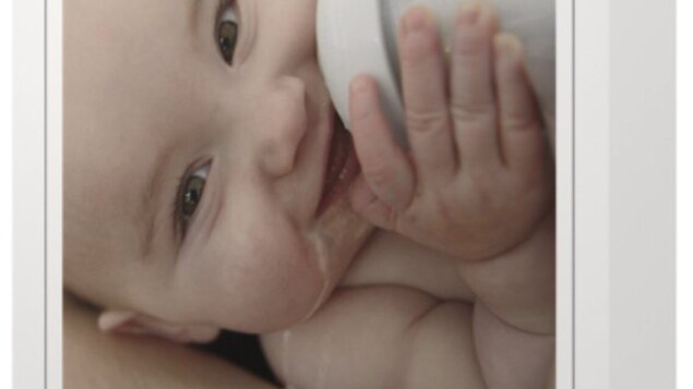 Un bébé souriant, biberon rempli de lait dans les mains