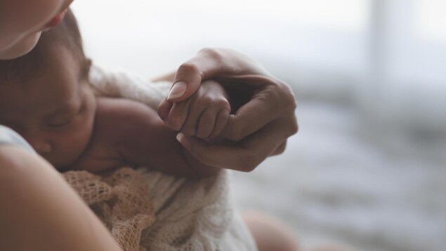 Une maman tient son nouveau-né dans ses bras, en lui tenant la main.