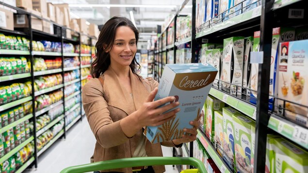 Une femme regarde une boîte de céréales dans le supermarché. 
