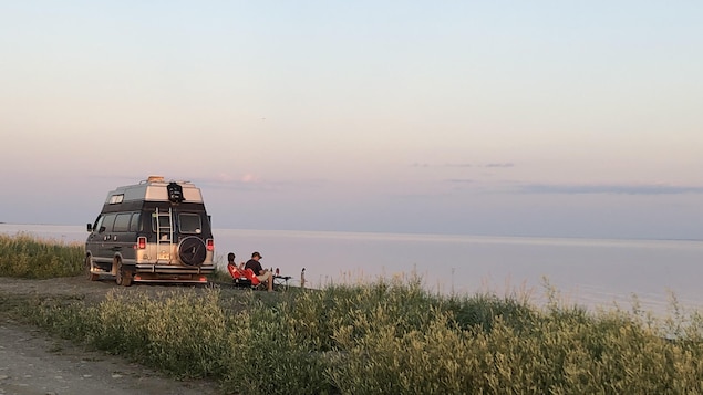 Deux personnes assises au bord de l'eau, à côté d'une roulotte.