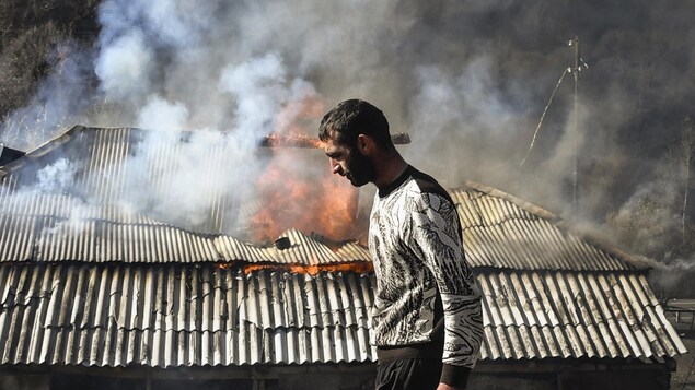 Un homme passe devant une maison en feu.