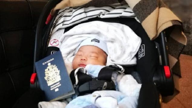 Un bébé dors dans un banc d'auto avec un passeport canadien.