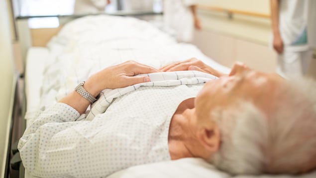 Un homme âgé est allongé sur une civière dans un couloir d'hôpital.
