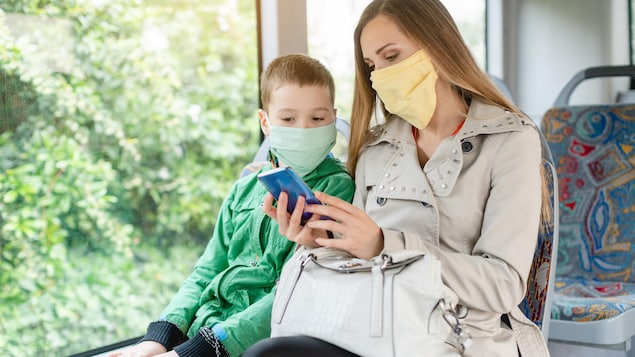 Une mère et son fils, vêtus de couvre-visages, consultent un téléphone intelligent.