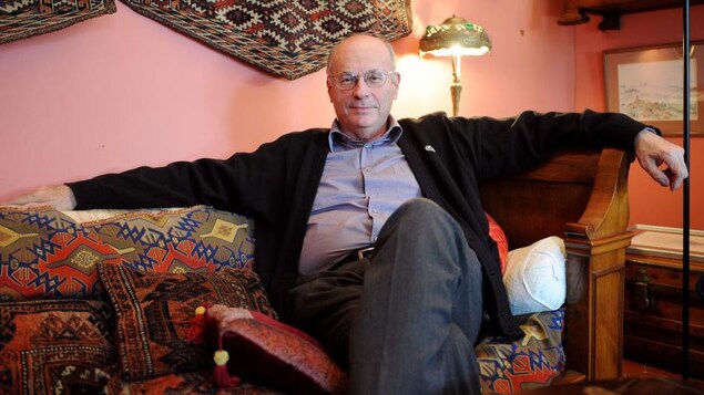 L'homme chauve est assis dans un salon, les bras étendus de chaque côté du sofa.