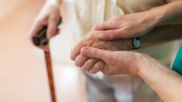 Gros plan sur les mains d'une femme tenant la main d'une personne âgée qui se déplace avec une canne. 
