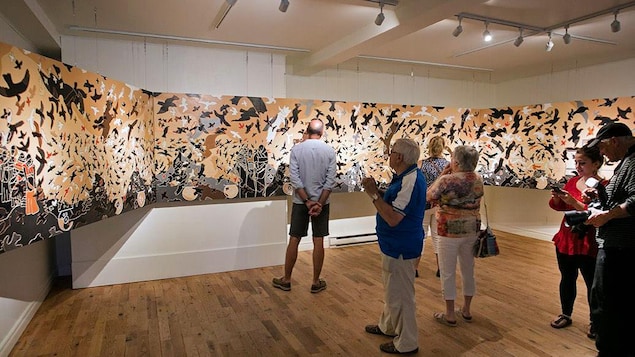 Six personnes sont devant une toile artistique dans un musée.