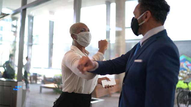 Une femme et un homme portant des masques dans un bureau se saluent en se touchant le coude. 