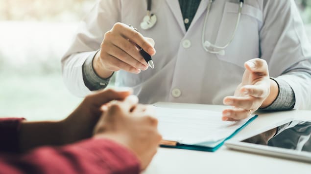 Les bras d'un médecin et de sa patiente; ils discutent, assis à un bureau.