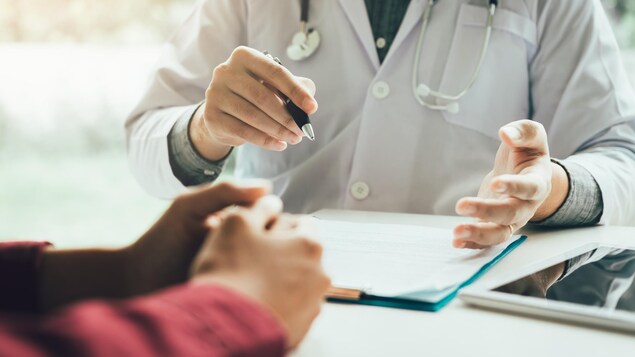 Les bras d'un médecin et de sa patiente discutant, assis à un bureau.