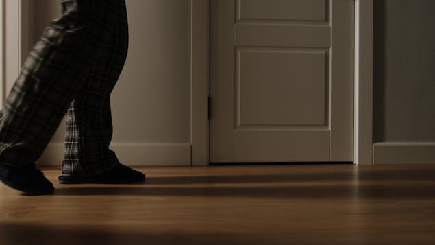 Vue des jambes d'un homme en pyjama déambulant dans un couloir sombre.