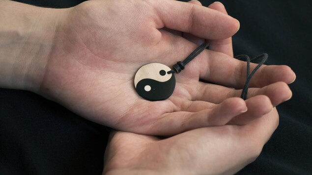 Gros plan sur les mains d'une personne tenant un médaillon à l'effigie du symbole Yin yang.
