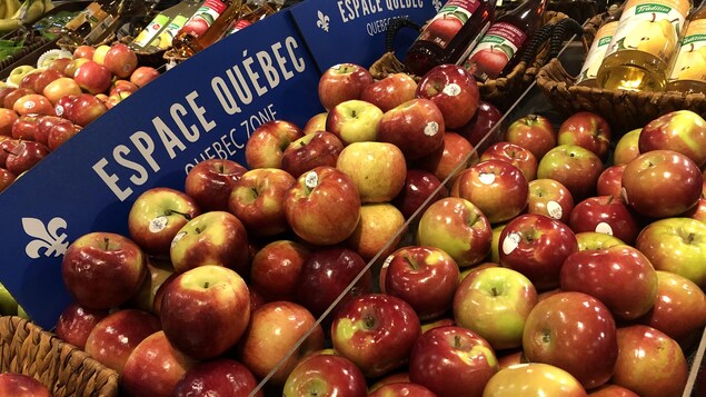 Des pommes dans un supermarché, devant une affiche « espace Québec »