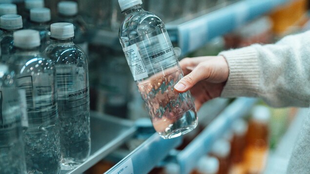 Gros plan de la main d'une personne qui tient une bouteille d'eau en plastique dans un supermarché. 