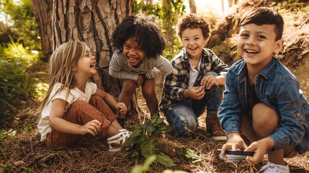 Quatre enfant sont accroupis dehors au pied d'un arbre et rient de bon coeur.