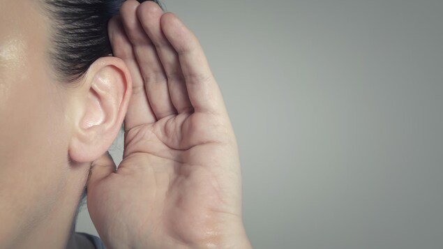 Une femme tend la main à son oreille pour mieux entendre.