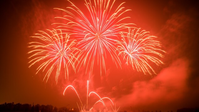 Un feu d'artifice rouge illumine le ciel et un lac. Un feu d'artifice rouge illumine le ciel et un lac.