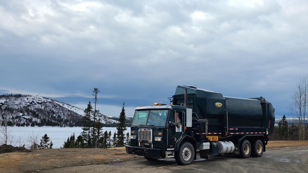 Un camion à ordures sur une route en gravier avec une montagne et un lac en arrière-plan