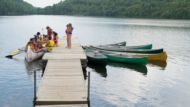 Des enfants sont sur le bout d'un quai et d'autres dans un canot sur le bord d'un lac