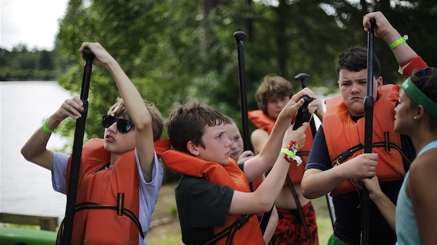 Des enfants dans un camp de vacances d'activités nautiques apprennent comment tenir leur pagaie, sous les conseils d'une monitrice.