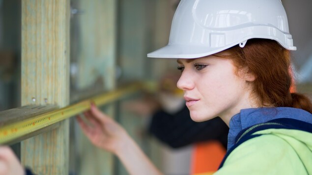 Une jeune femme charpentière utilise un ruban à mesurer sur un chantier de construction.