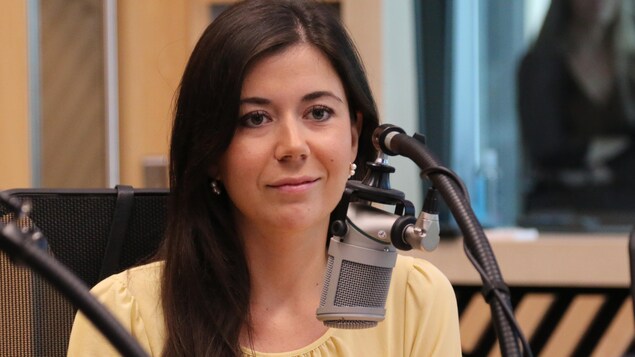 Une femme assise dans un studio de radio regarde en souriant dans la direction de l'animateur. 